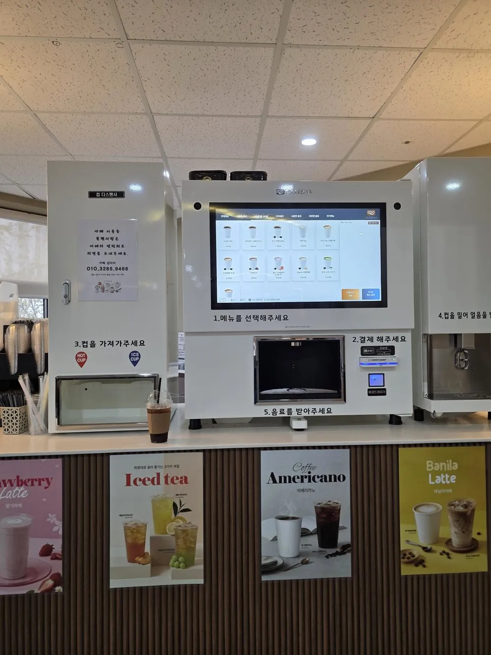 메뉴 포스터를 붙인 카운터 위의 유로 무인카페머신과 제빙기, 컵 디스펜서